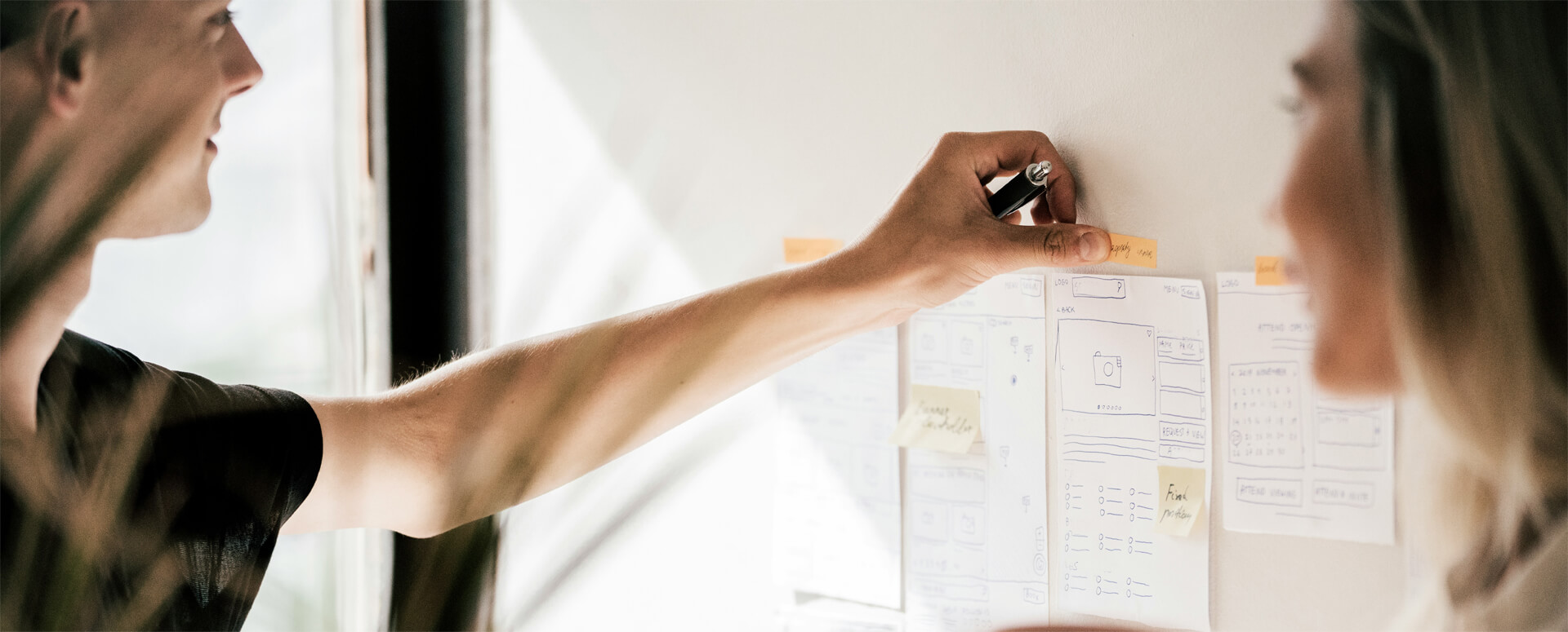 Eine Frau und ein Mann stehen an einer weißen Tafel und besprechen das weitere Vorgehen